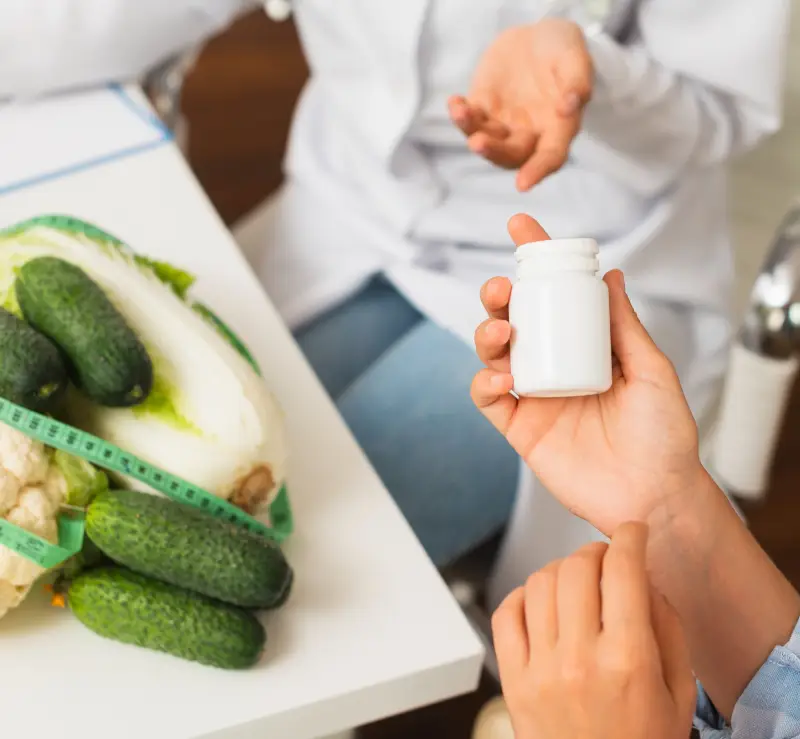 A hand holding a pill bottle next to some healthy foods